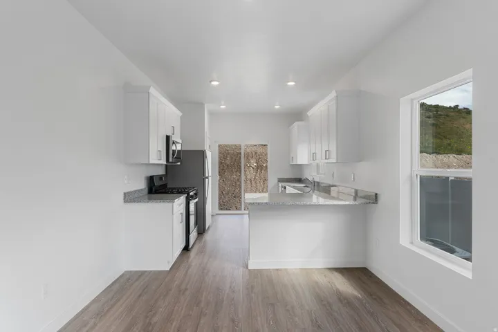 White cabinetry, stainless steel appliances, wood-finish flooring, recessed lighting, and a kitchen island with stone countertops