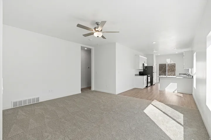 Open-concept living space featuring neutral carpeting, a ceiling fan, and white walls