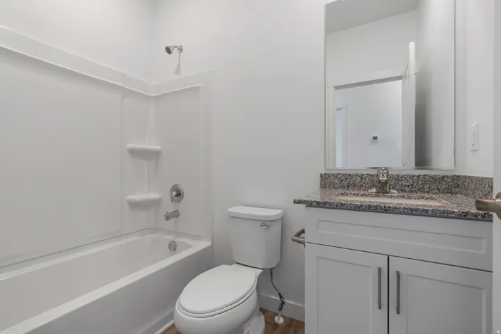 White bath/shower combination with chrome fixtures, wood-finish flooring, white vanity with shaker-style cabinetry, granite countertop, and rectangular mirror