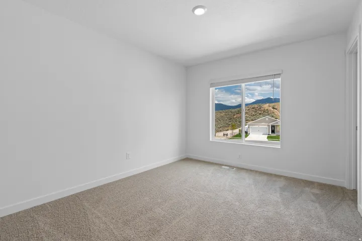 Recessed ceiling lighting, neutral carpet, white walls, large window with roller shade, mountain and residential scenery