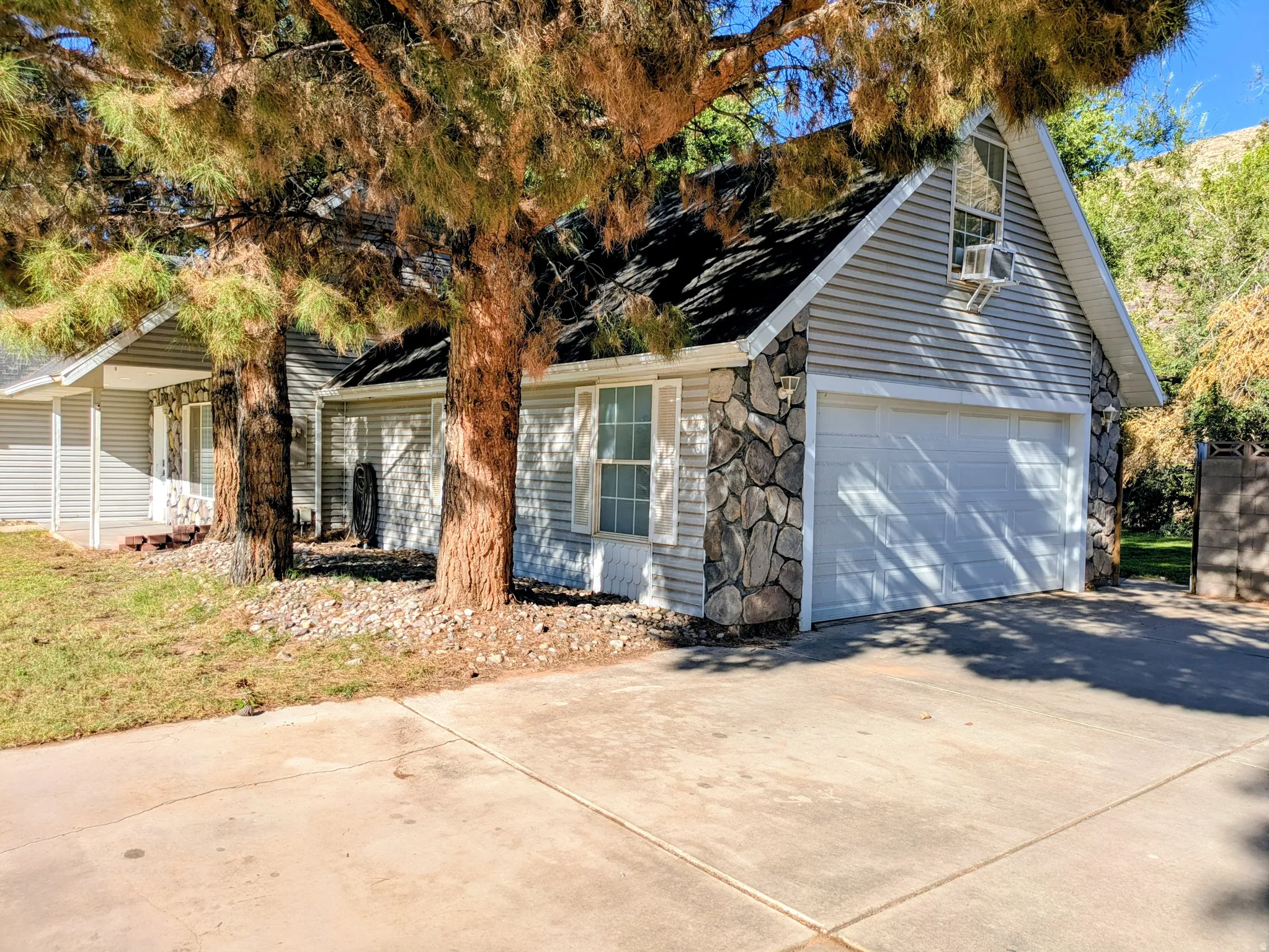 Stone facade accents, horizontal siding, attached garage, mature trees, and a concrete driveway