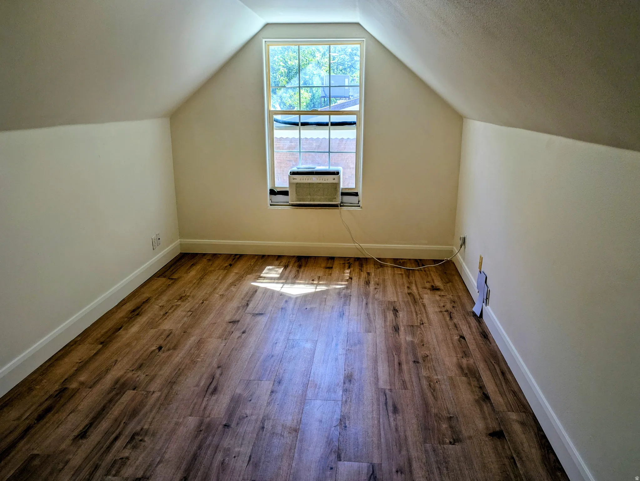 Vaulted ceilings with exposed beams, wood-finish flooring, and a window unit