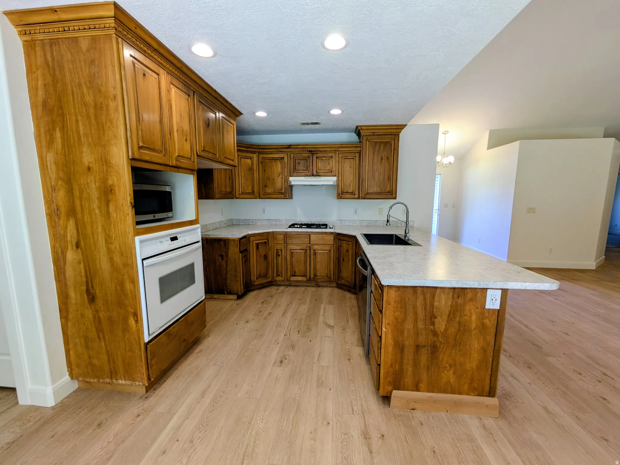 Kitchen featuring wood-finish cabinetry, light-toned countertops, built-in oven, recessed lighting, and wood-finish flooring