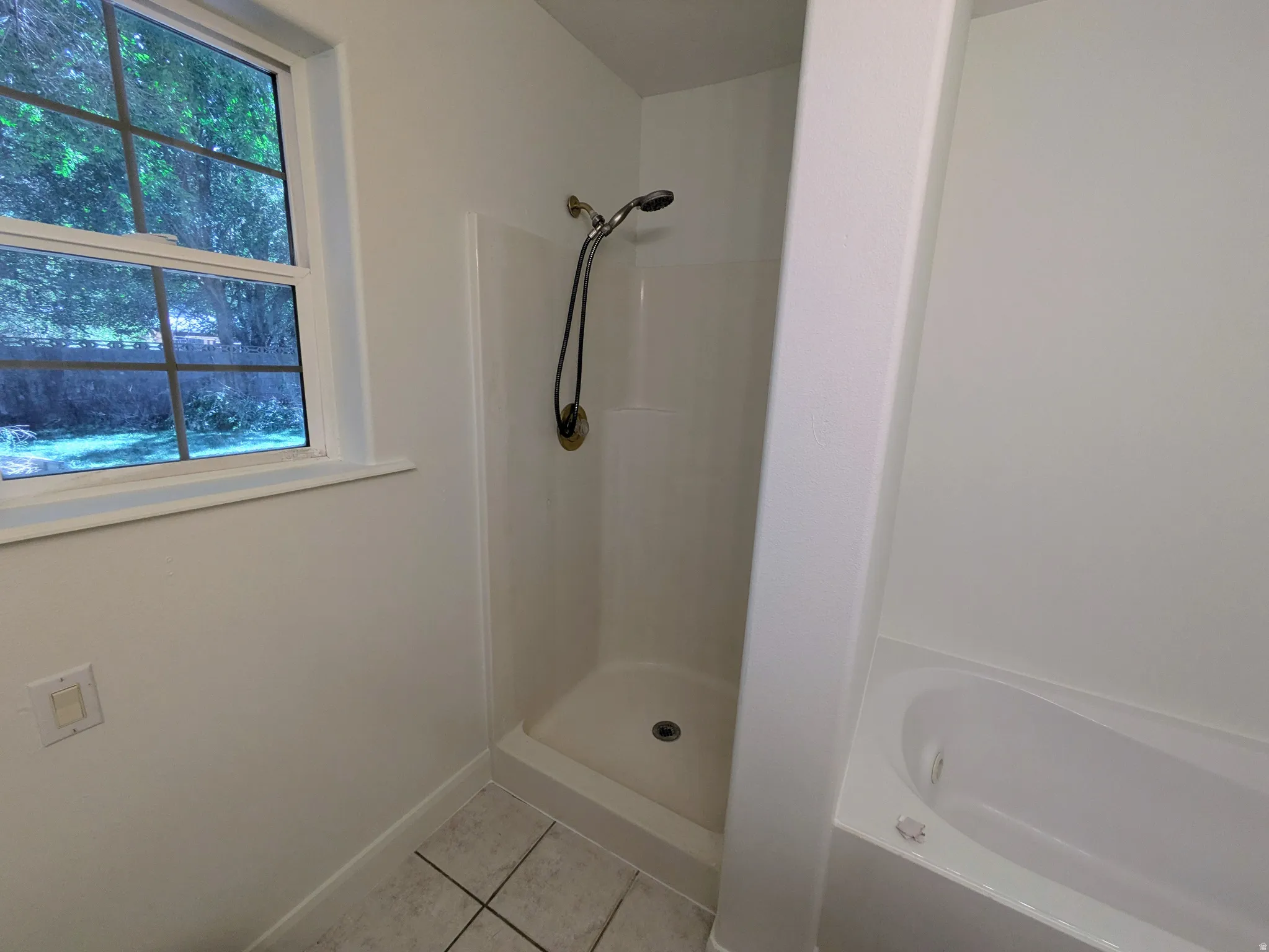 White paneled shower stall with a brushed nickel shower head, separate soaking tub, and a window with exterior visibility