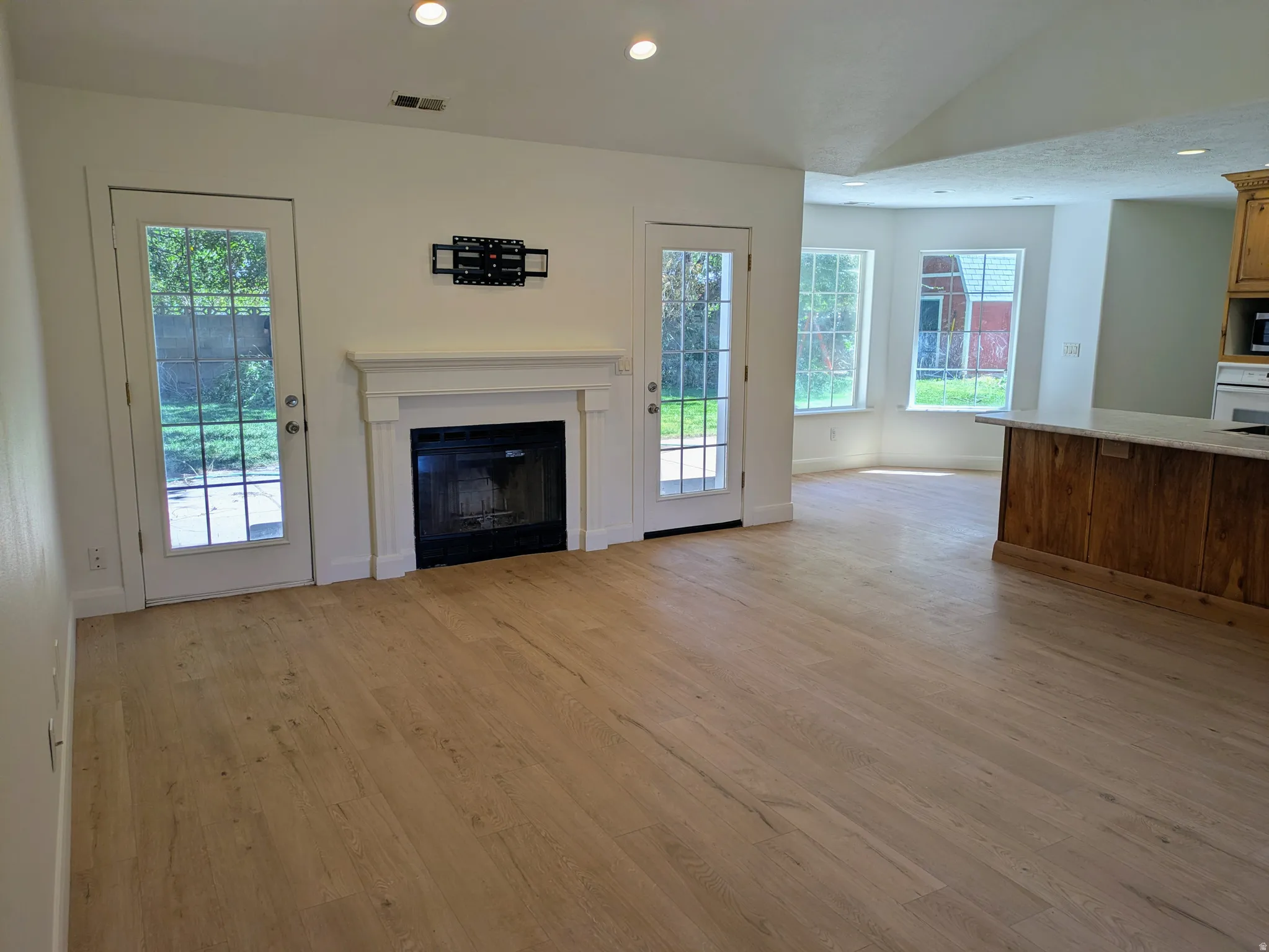 Open-concept living area with wood-finish flooring, a classic fireplace with white mantel, recessed lighting, and two glass-paneled doors