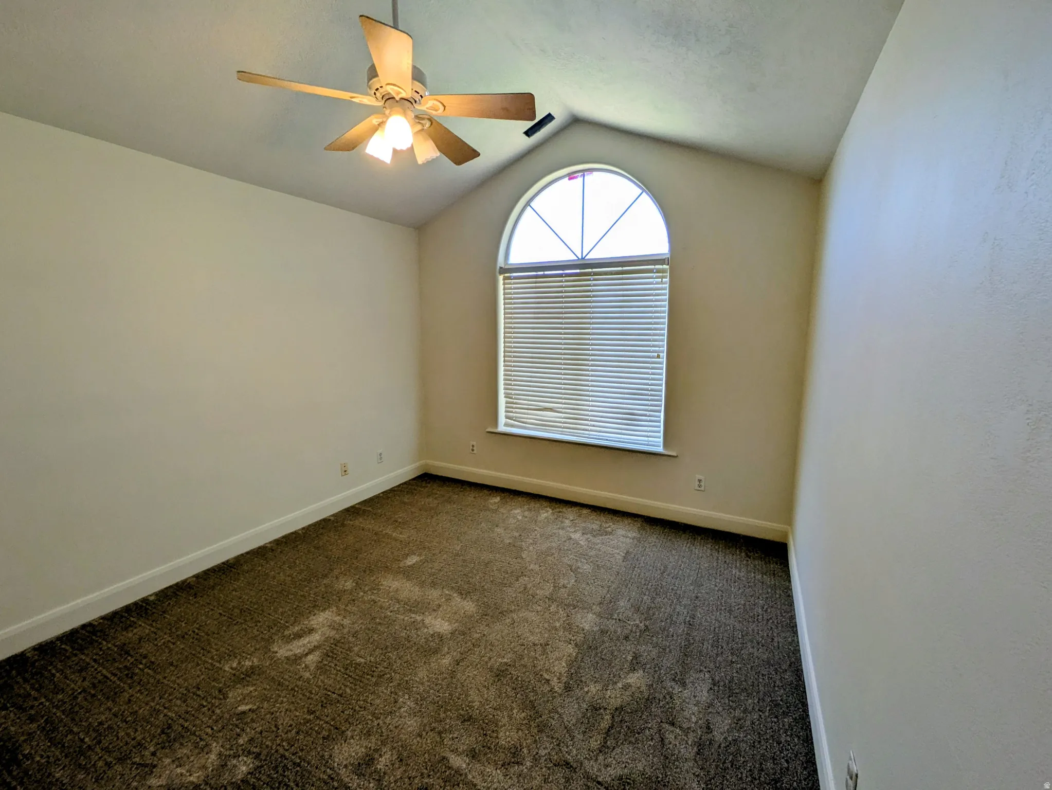 Vaulted ceiling with a ceiling fan, arched window with horizontal blinds, and wall-to-wall carpeting