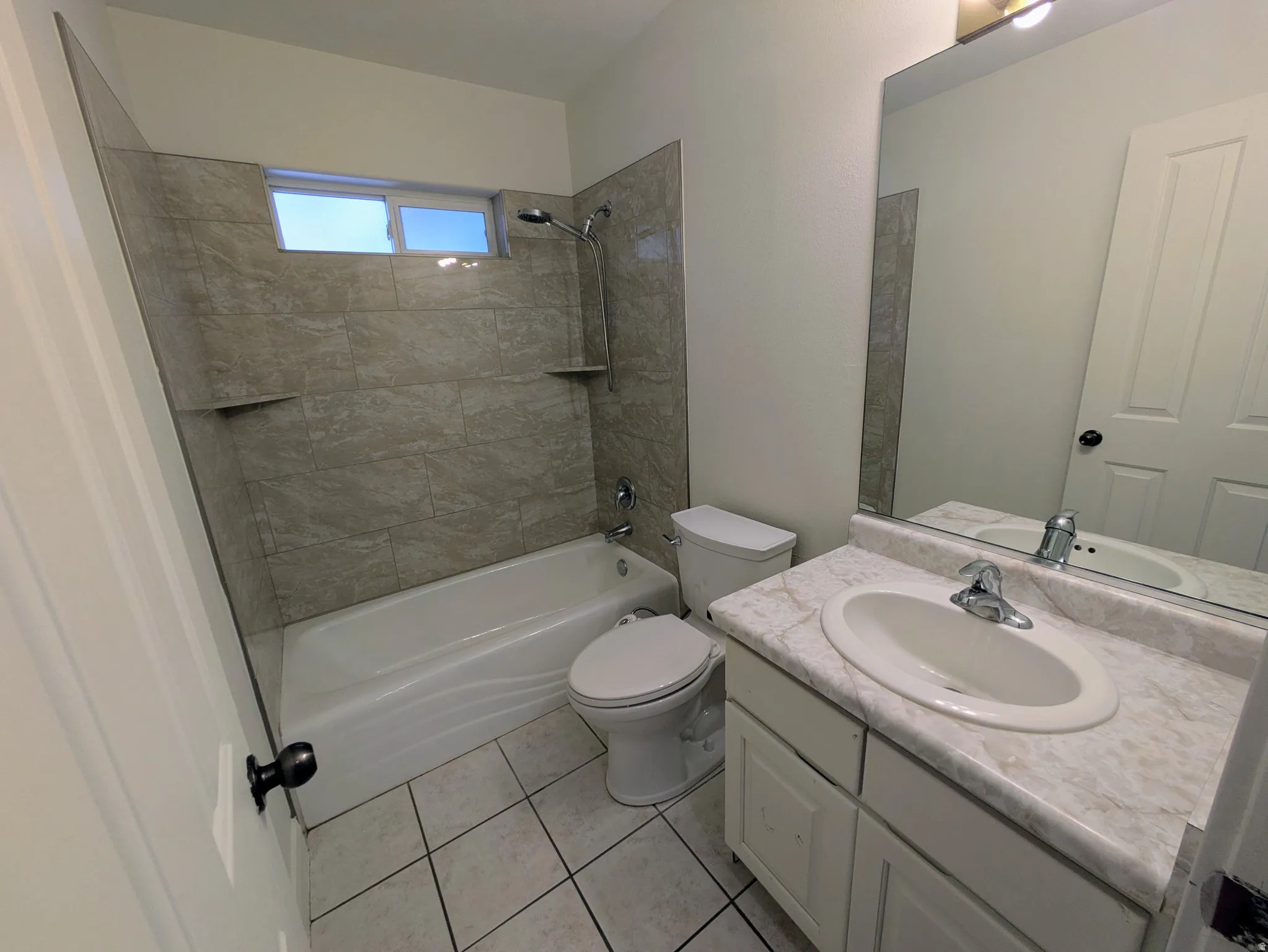 White vanity with integrated sink, stone-look countertop, large mirror, and tiled flooring