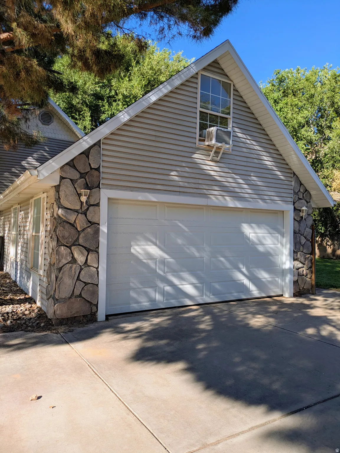 Two-car garage with white paneled door, stone veneer accents, and horizontal siding