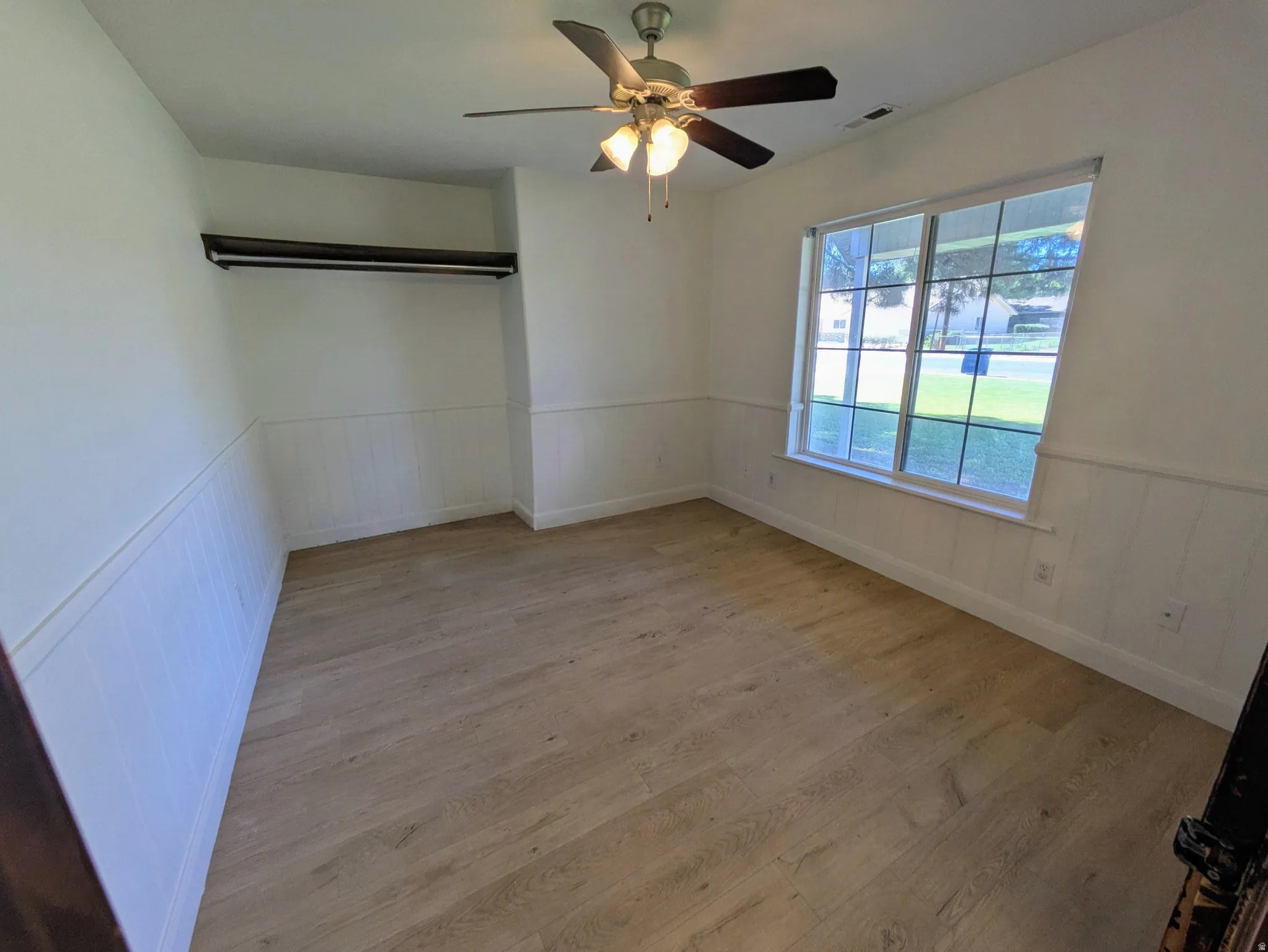 Light wood-finish flooring, white wainscoting, and a ceiling fan with integrated lighting