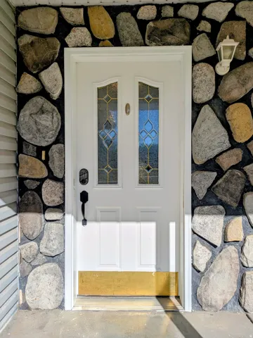 White entry door with decorative glass inserts, surrounded by a stone facade and featuring a wall-mounted exterior light fixture