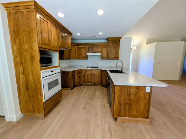Kitchen featuring wood-finish cabinetry, light-toned countertops, built-in oven, recessed lighting, and wood-finish flooring
