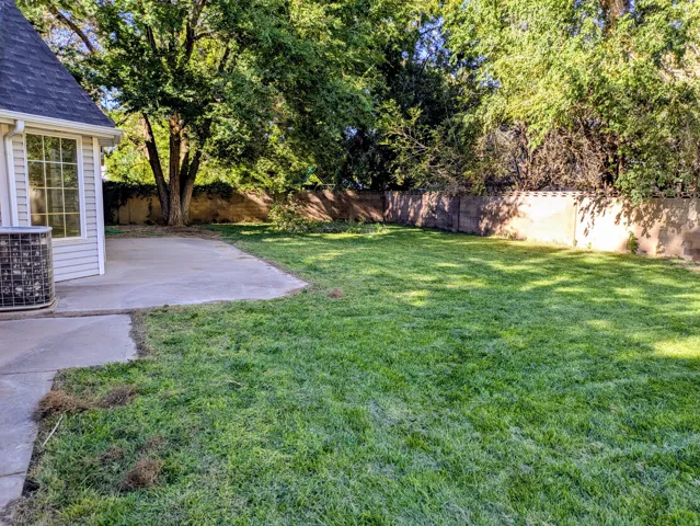 Expansive lawn area with mature trees, concrete patio, and perimeter fencing