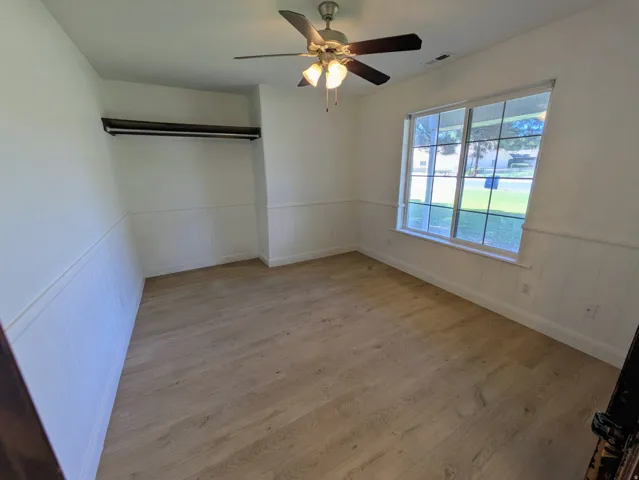 Light wood-finish flooring, white wainscoting, and a ceiling fan with integrated lighting