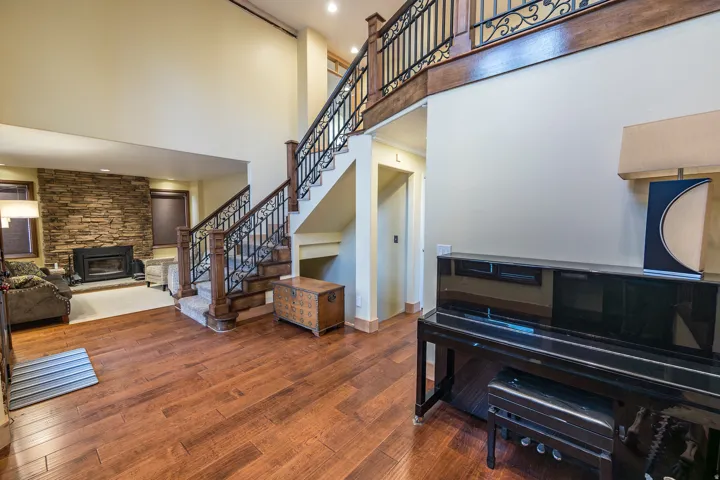 Two-story entry with wood-finish flooring, a grand staircase featuring wrought iron balusters and wood newel posts, and a stone-clad fireplace with a hearth