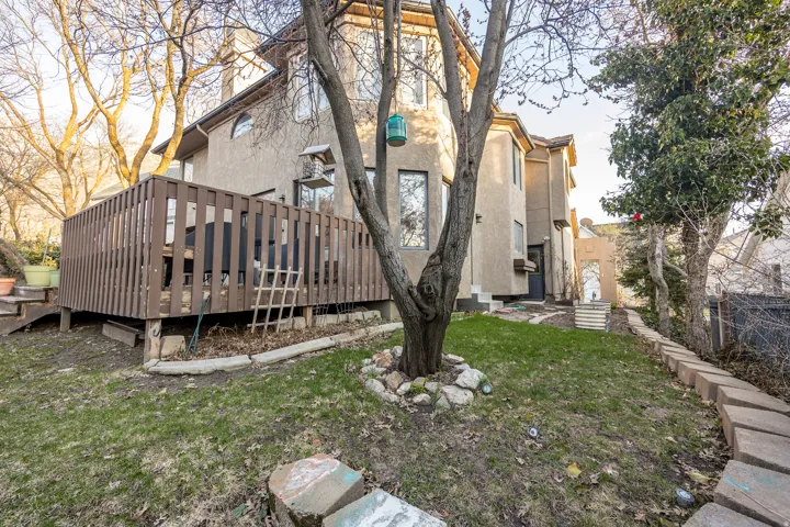 Exterior featuring stucco siding, multiple windows, a raised wooden deck with railings, and a sloped grassy area with stone-edged landscaping