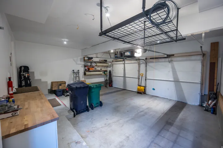 Attached garage featuring two overhead doors, overhead storage racks, recessed lighting, and a built-in workbench with a wood-finish top