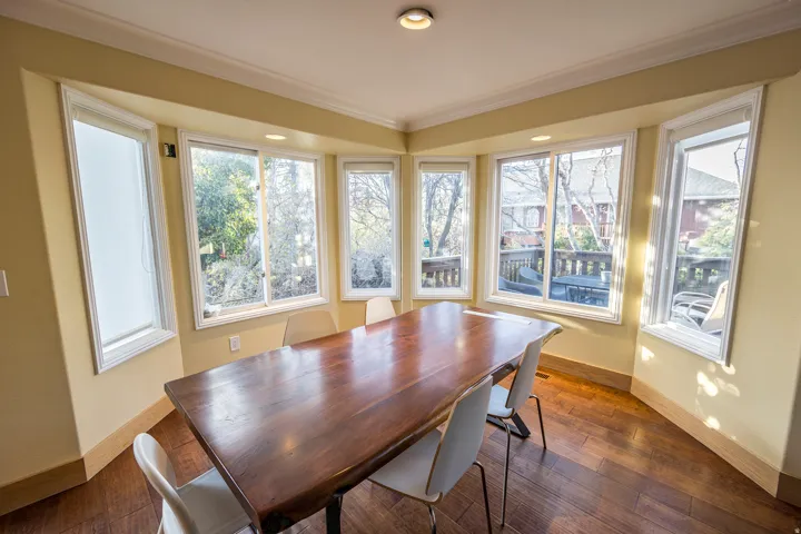 Sunlit sitting room featuring expansive multi-pane windows on three sides, warm yellow-painted walls, and rich wood-finish flooring throughout