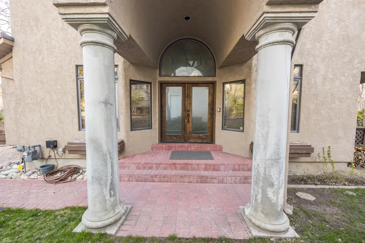 Stucco exterior with decorative columns, brick-paved entry, and double-door entrance featuring an arched transom window