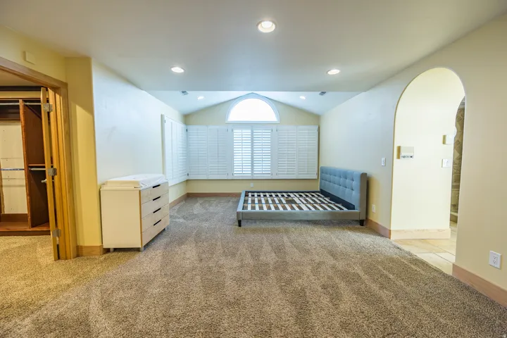 Room featuring carpet flooring, recessed lighting, plantation shutters, an arched entryway, and a bi-fold closet door