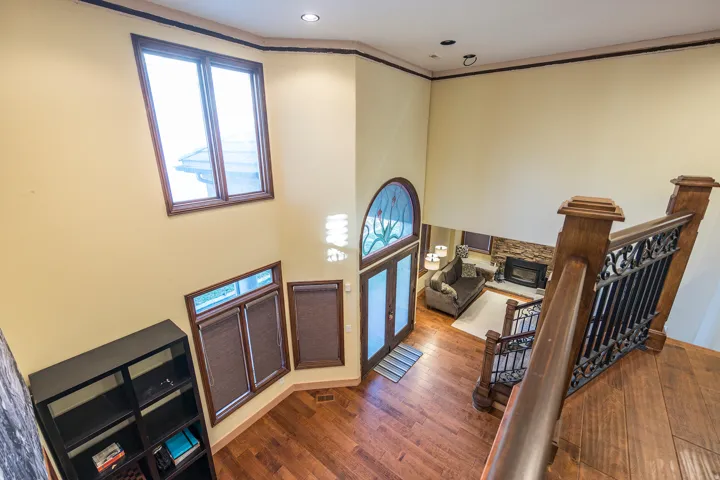 Vaulted ceiling, wood-finish flooring, ornate wrought iron staircase, arched transom window, and stone-clad fireplace