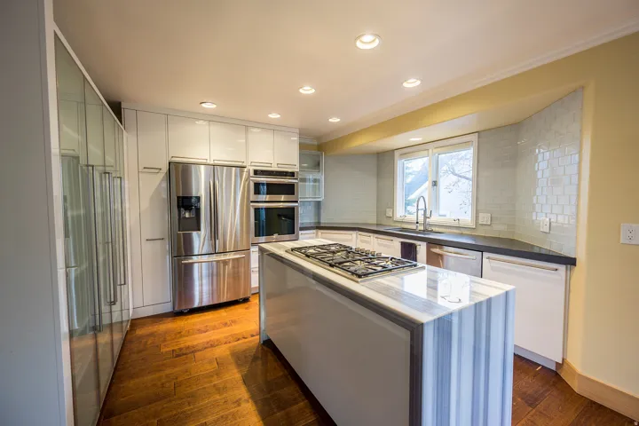 Kitchen featuring wood-finish flooring, white cabinetry, stainless steel appliances, and a central island with a gas cooktop and waterfall countertop