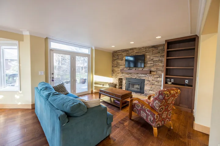 Stacked stone fireplace with a wood mantle, built-in shelving, wood-finish flooring, recessed lighting, and French doors