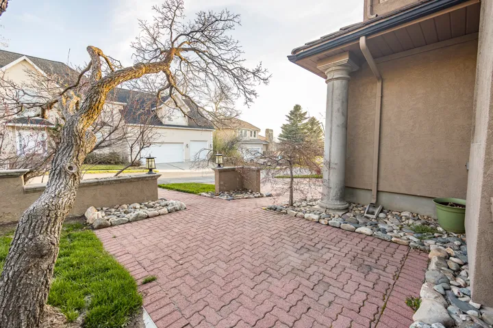 Brick paver entryway with decorative rock landscaping, stucco exterior, and a classical column accent