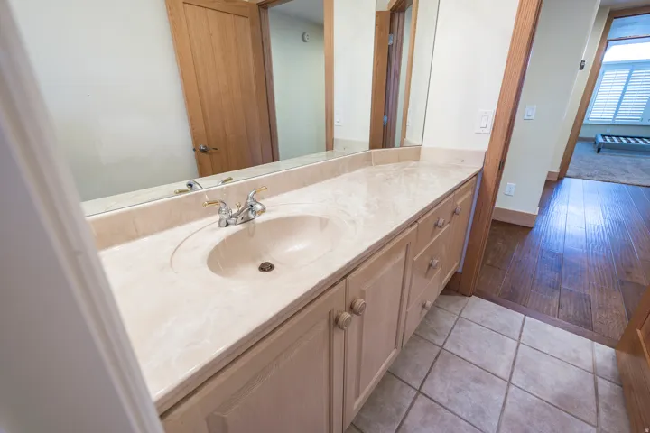 Vanity with an integrated sink and backsplash, set over a cabinet with storage drawers and doors, tile flooring, and a mirrored wall