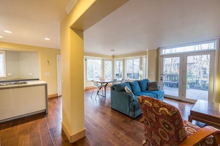 Wood-finish flooring throughout, featuring a kitchen island with cooktop, recessed lighting, a bay window with multiple panes, and double glass doors opening to the exterior