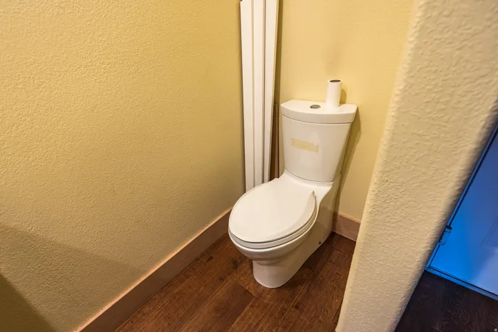 White two-piece toilet, wood-finish flooring, and light-colored textured wall