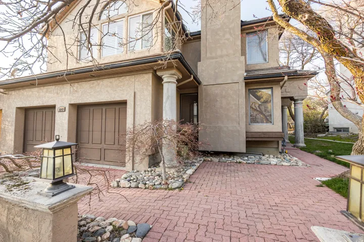 Stucco exterior with multiple windows, two garage doors, and a brick paver driveway