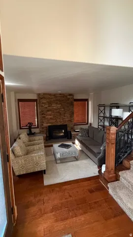 Living area featuring wood-finish flooring, a stone-clad fireplace, and a wood newel post with wrought iron balusters
