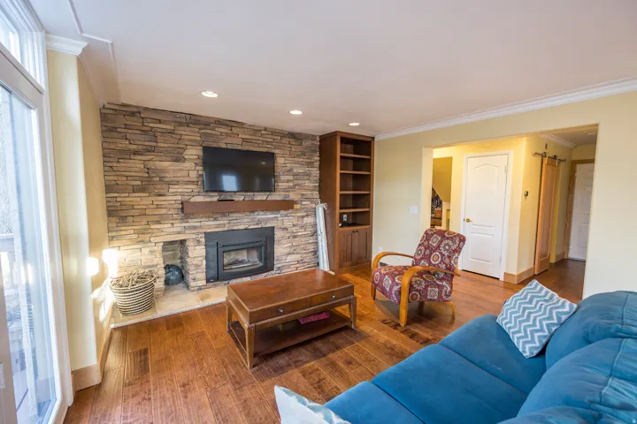 Stone-clad fireplace with a wood mantel, built-in wooden shelving, recessed lighting, and wood-finish flooring