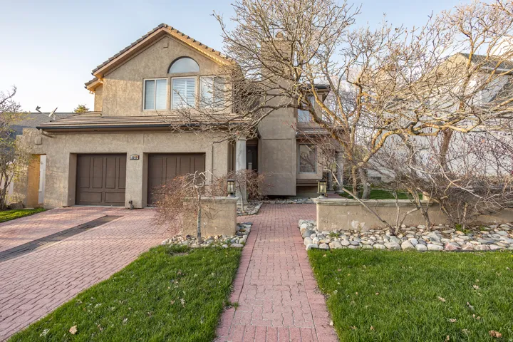 Stucco exterior with a two-car garage, arched window, and red paver driveway