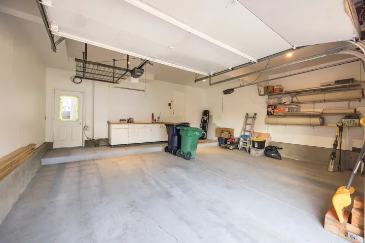 Attached garage with concrete flooring, built-in cabinetry, overhead storage, and wall-mounted shelving