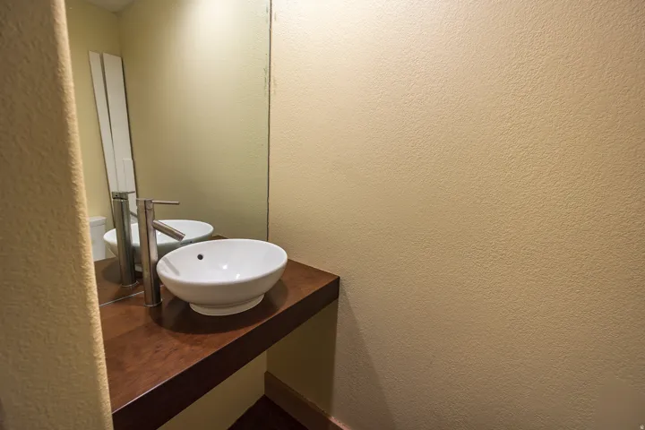 Floating wood-finish vanity with a vessel sink and a tall, polished chrome faucet