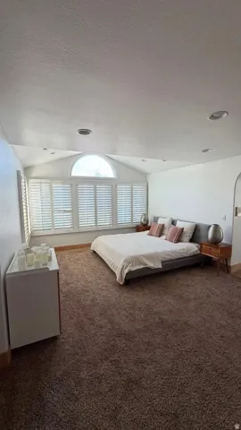 Vaulted ceilings, arch-top window, multiple windows with plantation shutters, recessed lighting, and rich brown carpeting