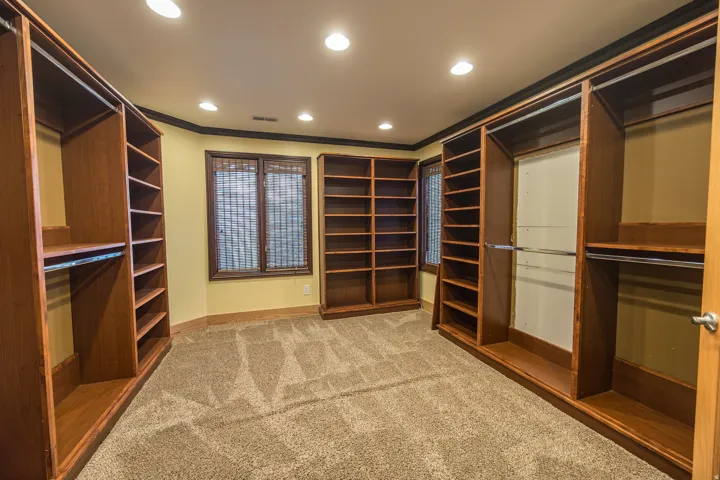 Custom wood-finish built-in shelving, integrated hanging rods, recessed ceiling lighting, and a textured carpet floor