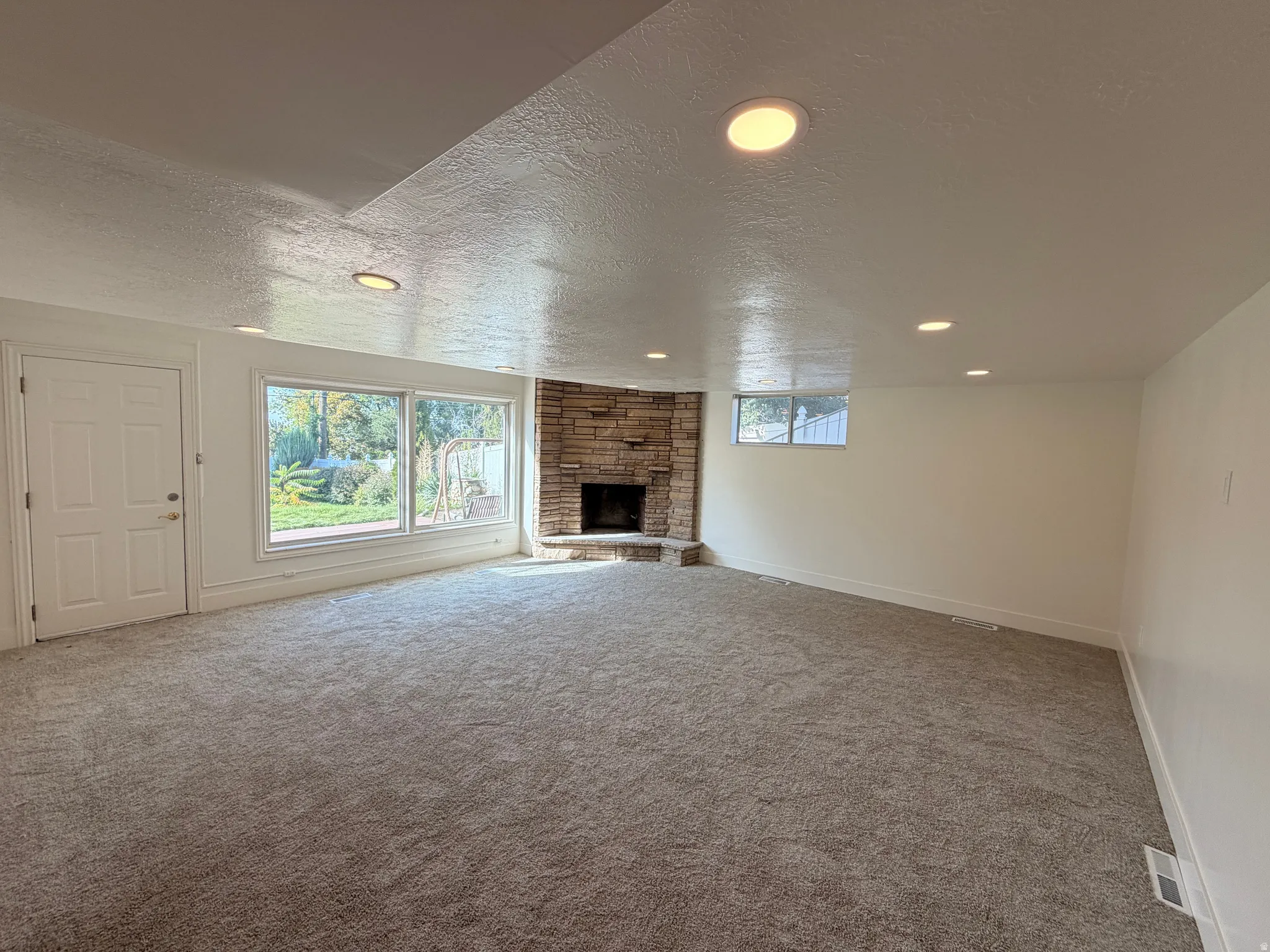Spacious room with recessed lighting, stone fireplace, large picture windows, and light-toned carpeting