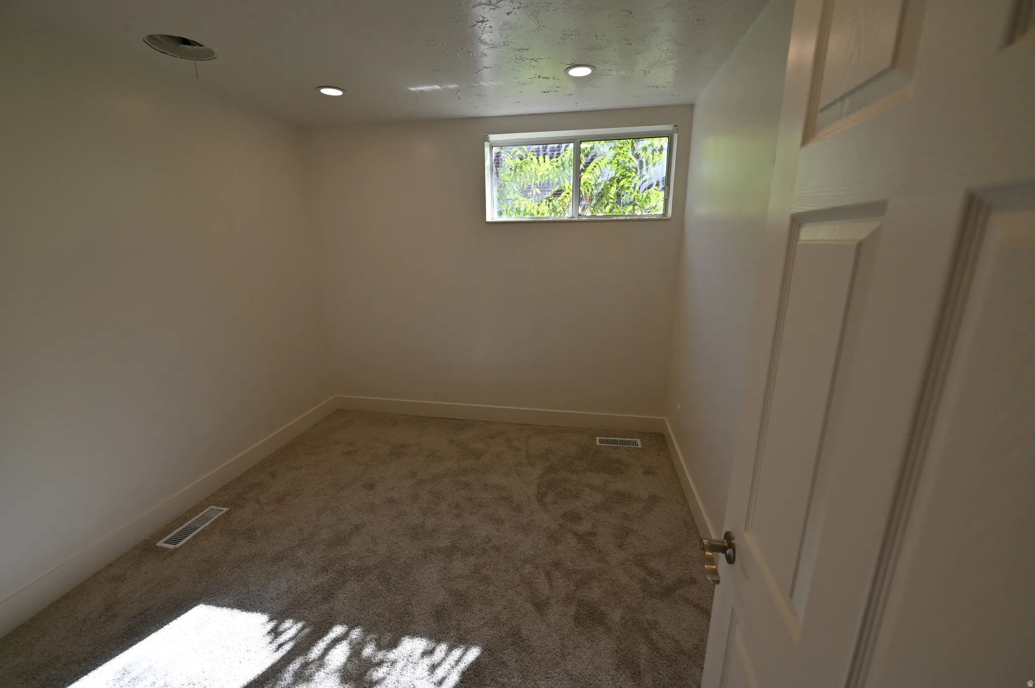 Carpeted room featuring a single window, recessed lighting, and a paneled interior door
