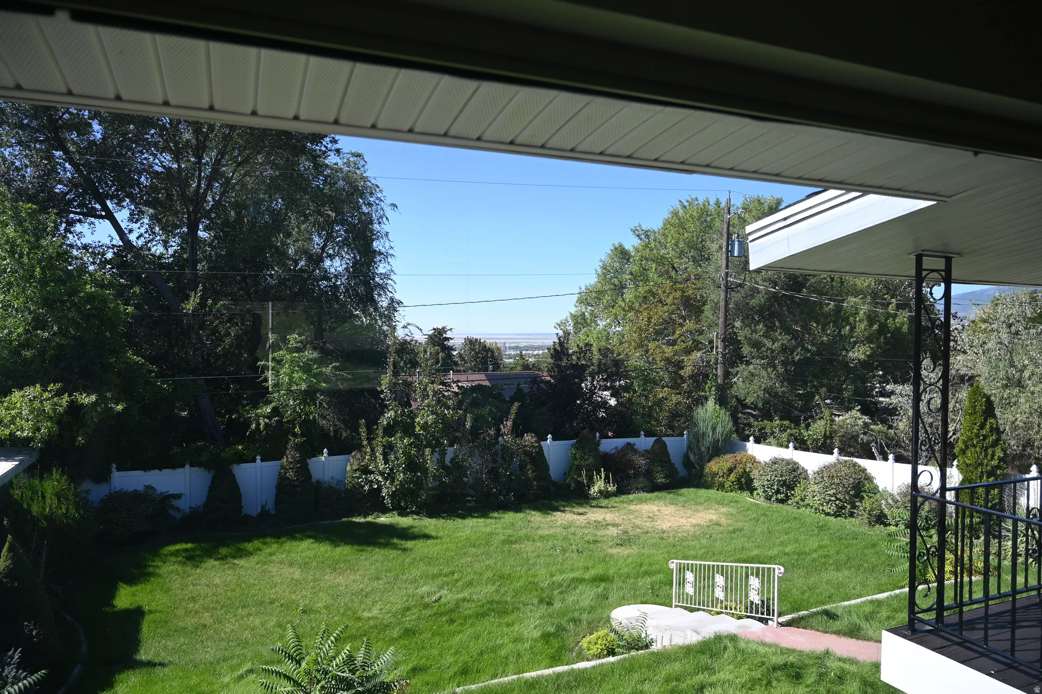 Expansive backyard featuring a manicured lawn, mature trees, and a white privacy fence