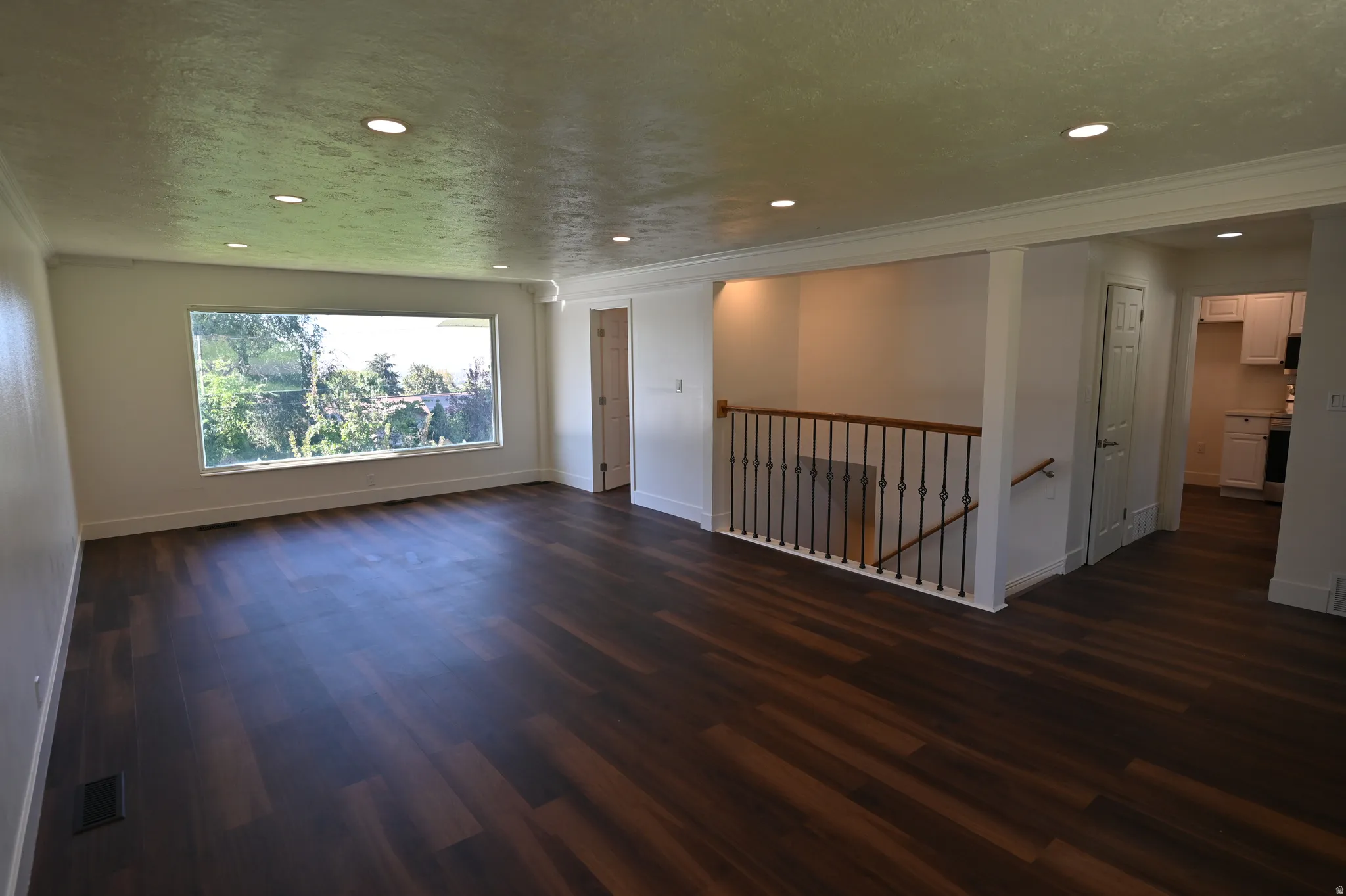Spacious open-concept loft featuring rich wood-finish flooring throughout, recessed ceiling lighting, and large picture window with natural light