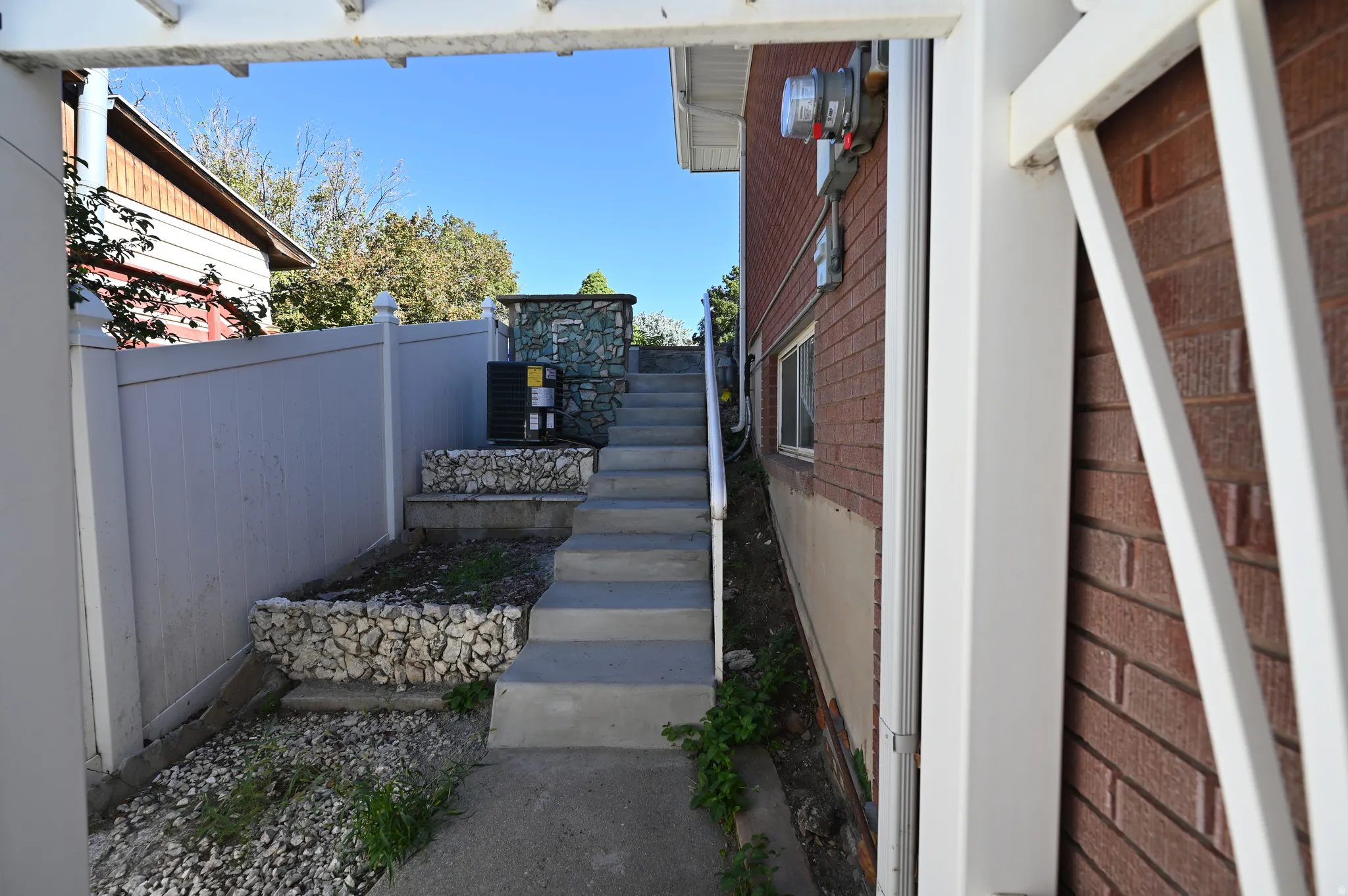 Concrete staircase with a metal handrail, stone-lined planters, and a privacy fence