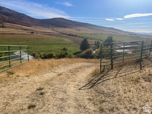 Expansive open land with rolling hills, fenced perimeter, and distant structures