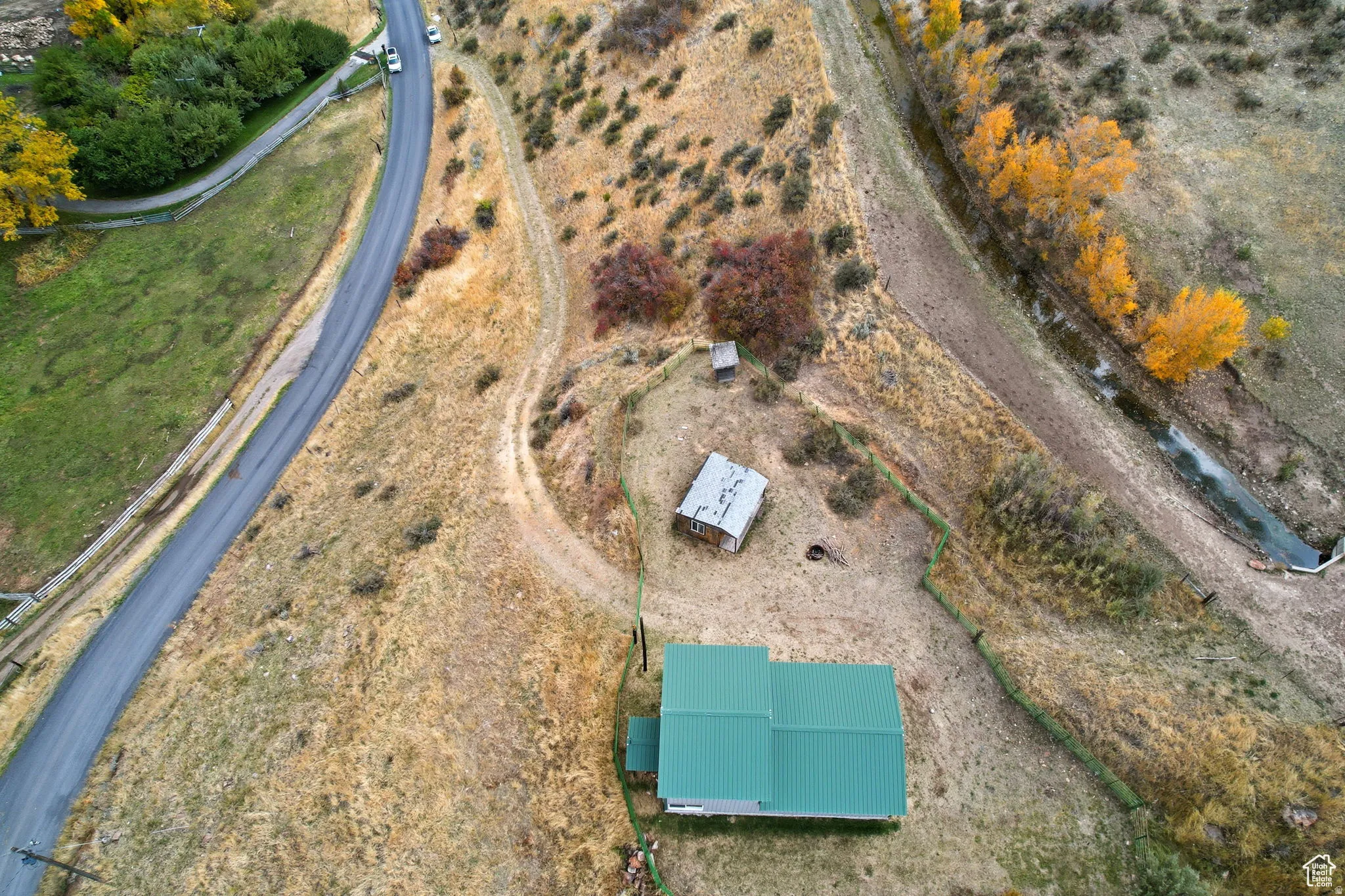Rural property featuring a green-roofed structure, secondary outbuilding, and nearby paved road