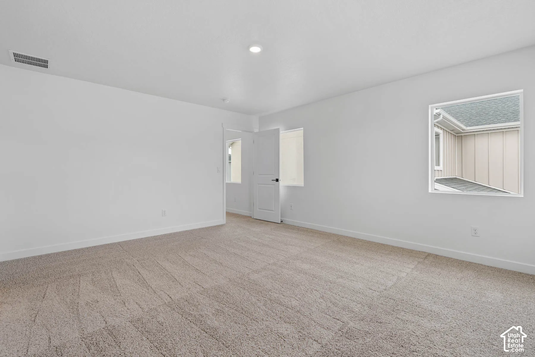 Spacious room featuring neutral carpeting, white walls, recessed lighting, and multiple windows for natural illumination