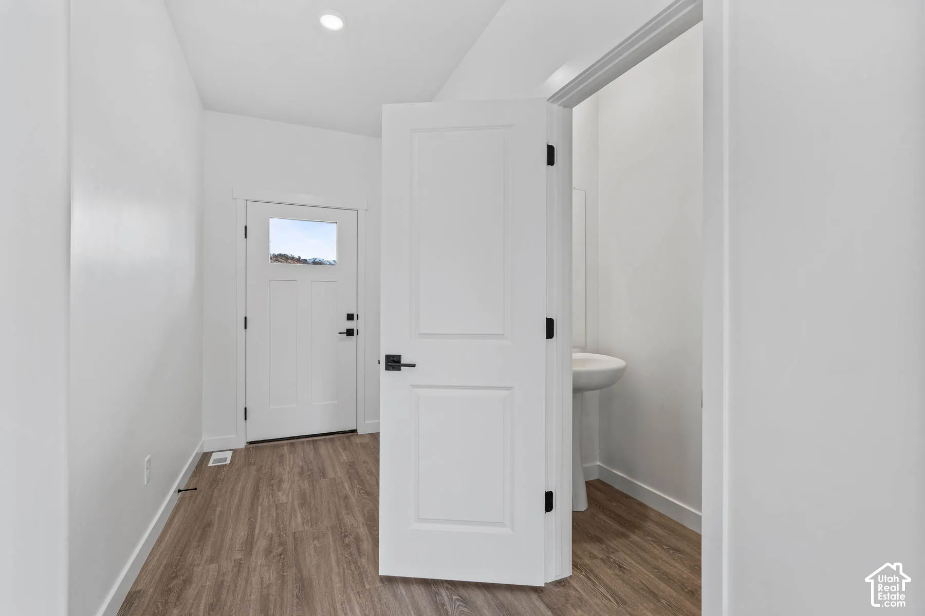 Entryway featuring wood-finish flooring, a white paneled door with matte black hardware, and a recessed ceiling light