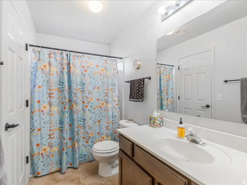 Bathroom featuring a single vanity with an integrated sink, wood-finish cabinetry, a large wall-mounted mirror, and tile flooring