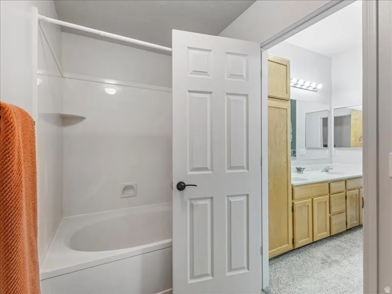 White paneled door separating areas, integrated shower/tub combination, and dual sink vanity
