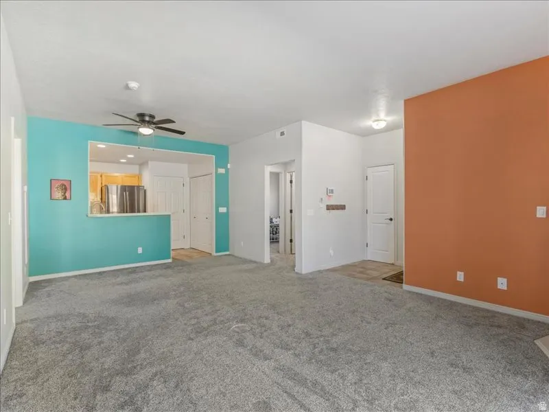 Gray carpeted flooring, a kitchen pass-through with a breakfast bar, a ceiling fan, and accent walls